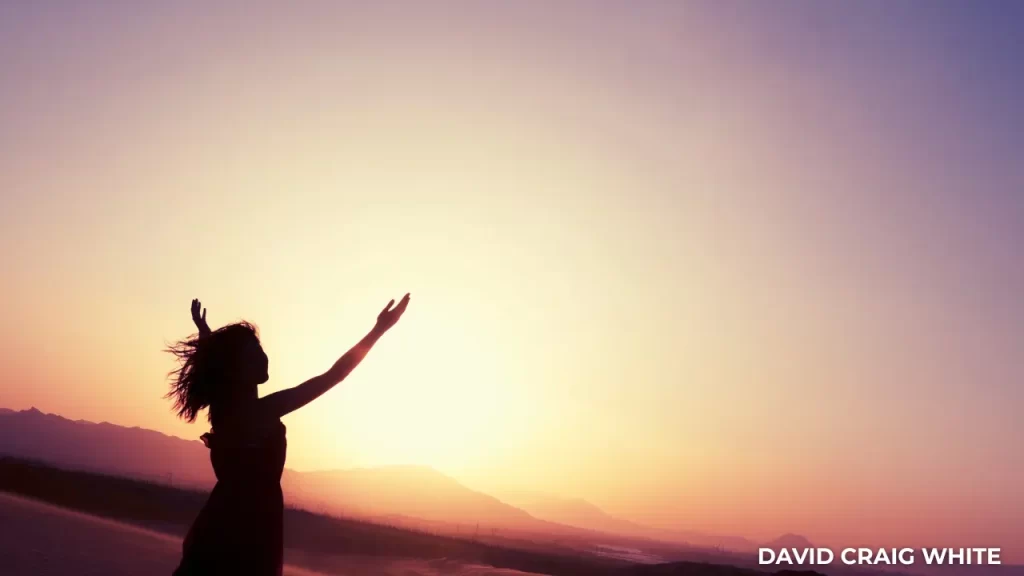 Silhouette of a woman with open arms at sunset, symbolising freedom and a simplified approach to work.