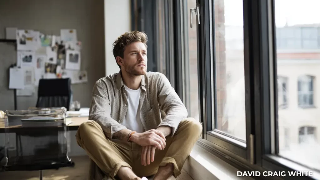 Small business owner sitting by a window, reflecting on business decisions